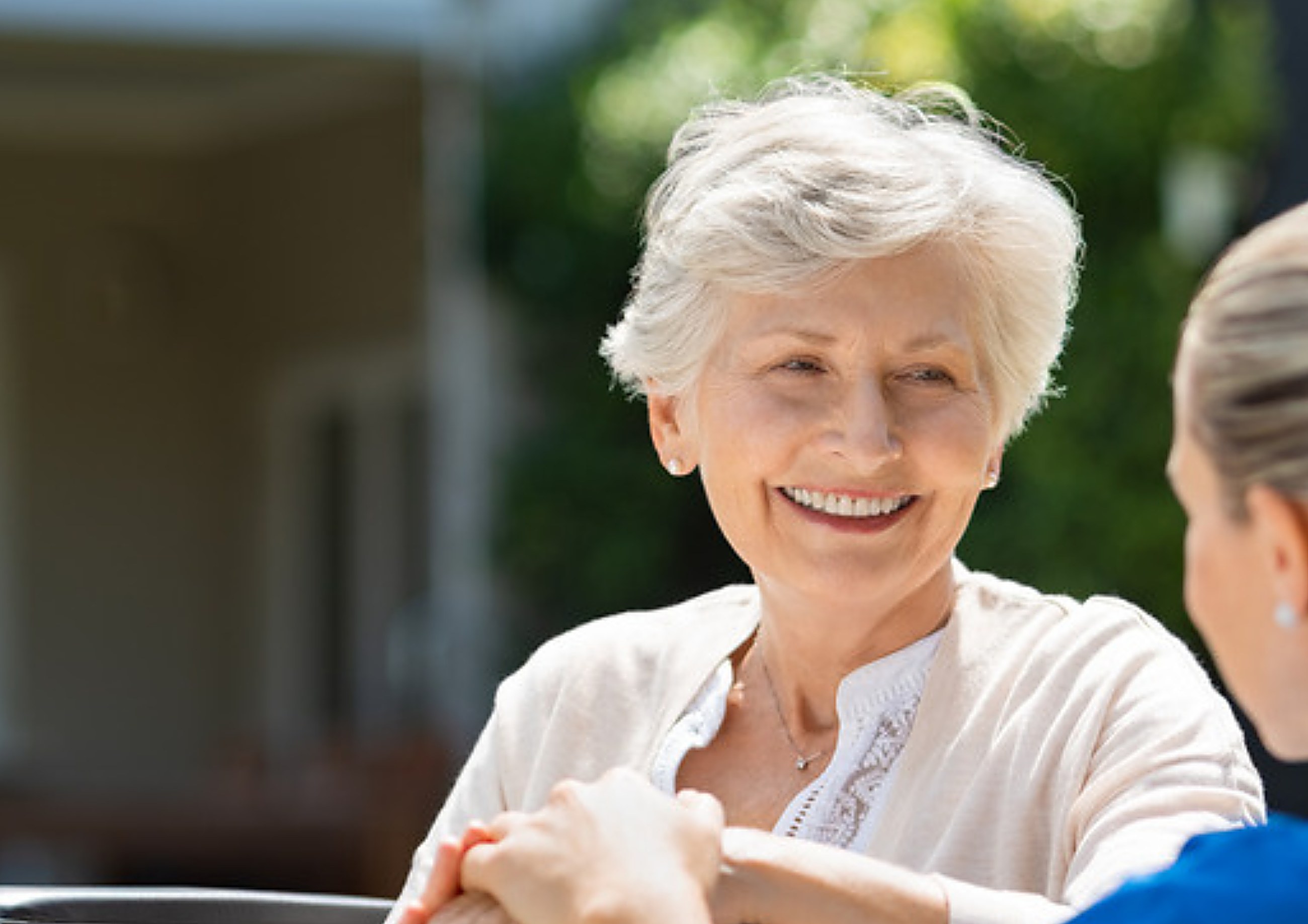 A smiling elderly resident with her carer in a care home garden